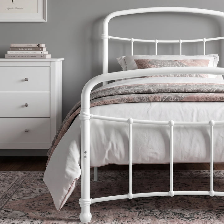 [White | Single] Close view of the white curved front rail, vertical bars and white bedding beside a drawers