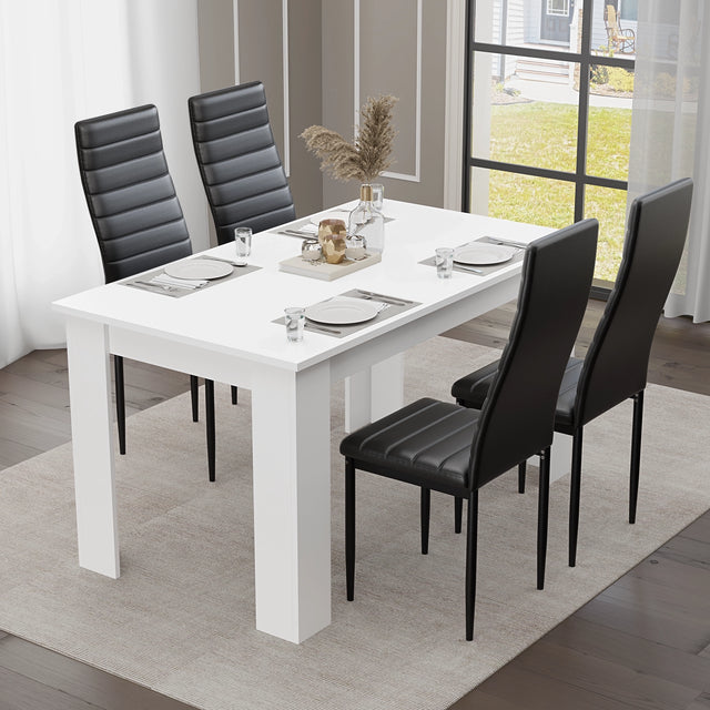 Modern white dining table set for four, paired with sleek black chairs. Styled in a contemporary dining room featuring elegant wall art and a statement chandelier — ideal for small families or compact spaces.