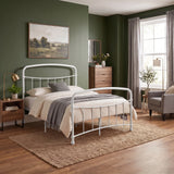 [White | Double] Wide bedroom scene showing curved bed rails, armchair, drawer chest, mirror, floor lamp, plants, and window.