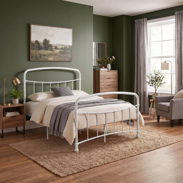 [White | Double] Wide bedroom scene showing curved bed rails, armchair, drawer chest, mirror, floor lamp, plants, and window.