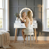 [White] Dressing table lifestyle shot with model seated at LED mirror applying makeup in a styled bedroom