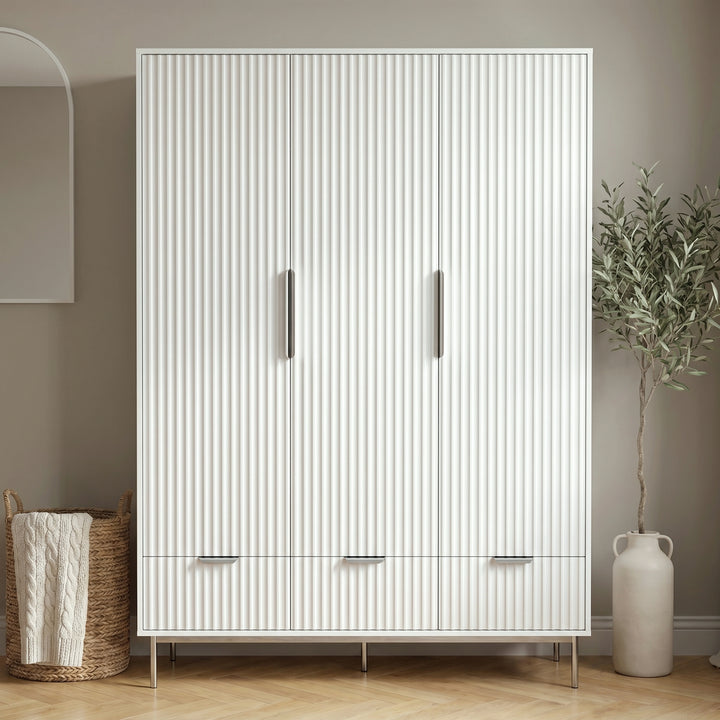 [White] Flutrina three door wardrobe front view with fluted panels, silver handles, three drawers and slim metal legs
