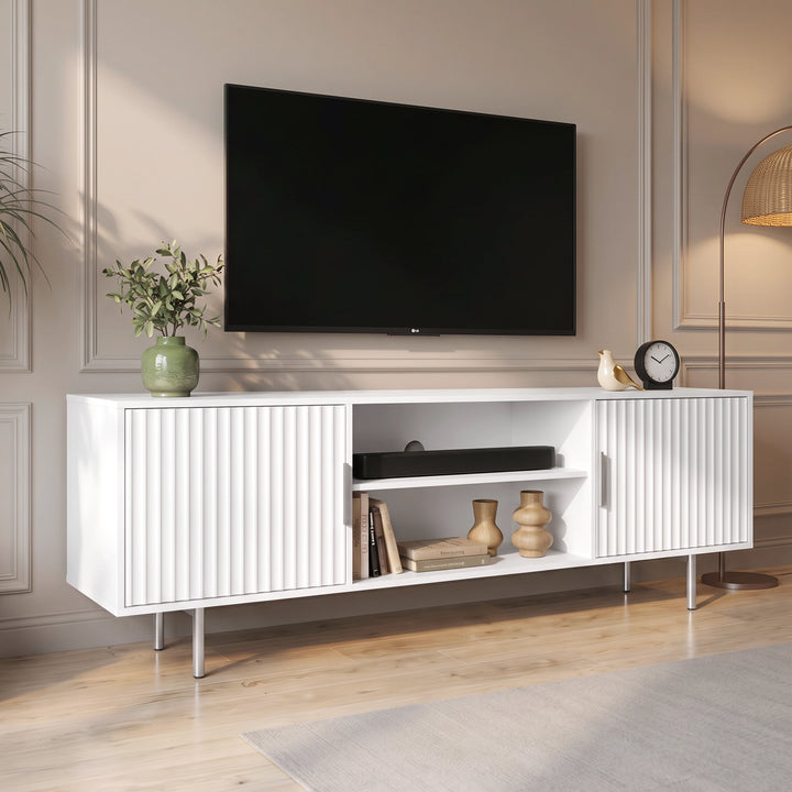 [White] Flutrina TV unit angled view with wall TV, fluted doors, open media shelf, books, vases, plant, lamp, and wood floor.