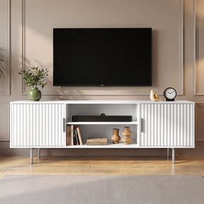 [White] Flutrina TV unit front view with fluted doors, open shelves, wall TV, plant, clock, bird ornament, books, and vases.