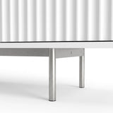 [White] Flutrina lower detail showing fluted door grooves, metal support rail, round silver legs, glides, and base edge.
