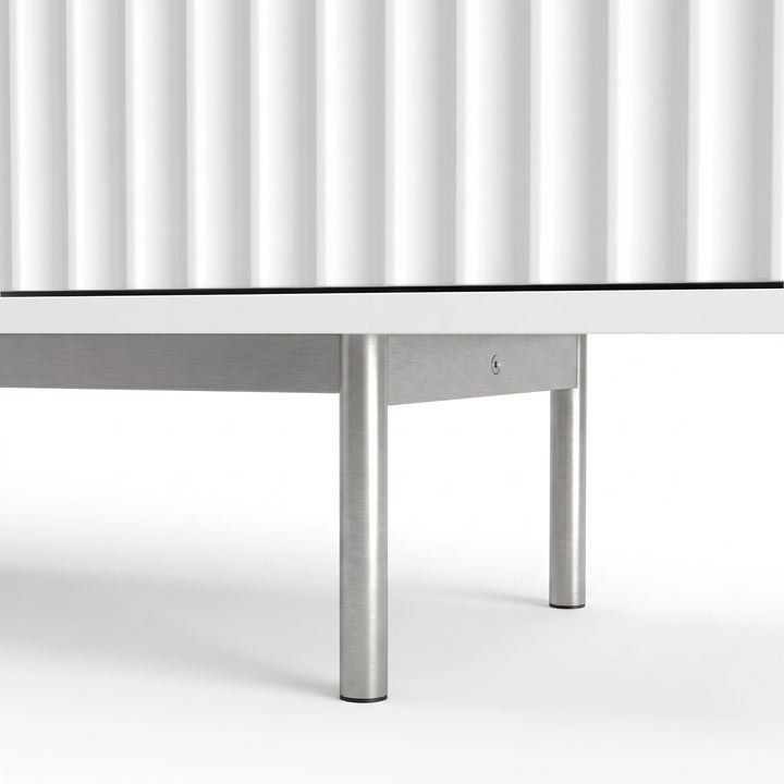 [White] Flutrina lower detail showing fluted door grooves, metal support rail, round silver legs, glides, and base edge.