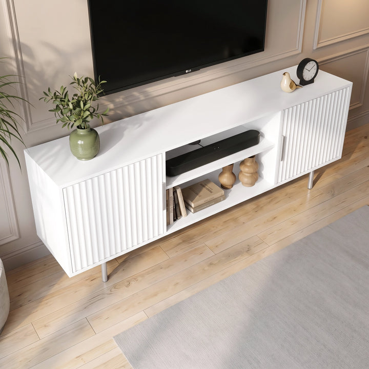 [White] Flutrina TV unit top-angle view showing fluted doors, open shelf, soundbar, books, vases, plant, and wood floor.