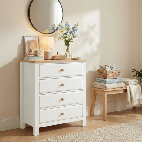 [White] Haven 4 drawer chest in a styled bedroom with a round mirror above, glowing table lamp and blue floral stems