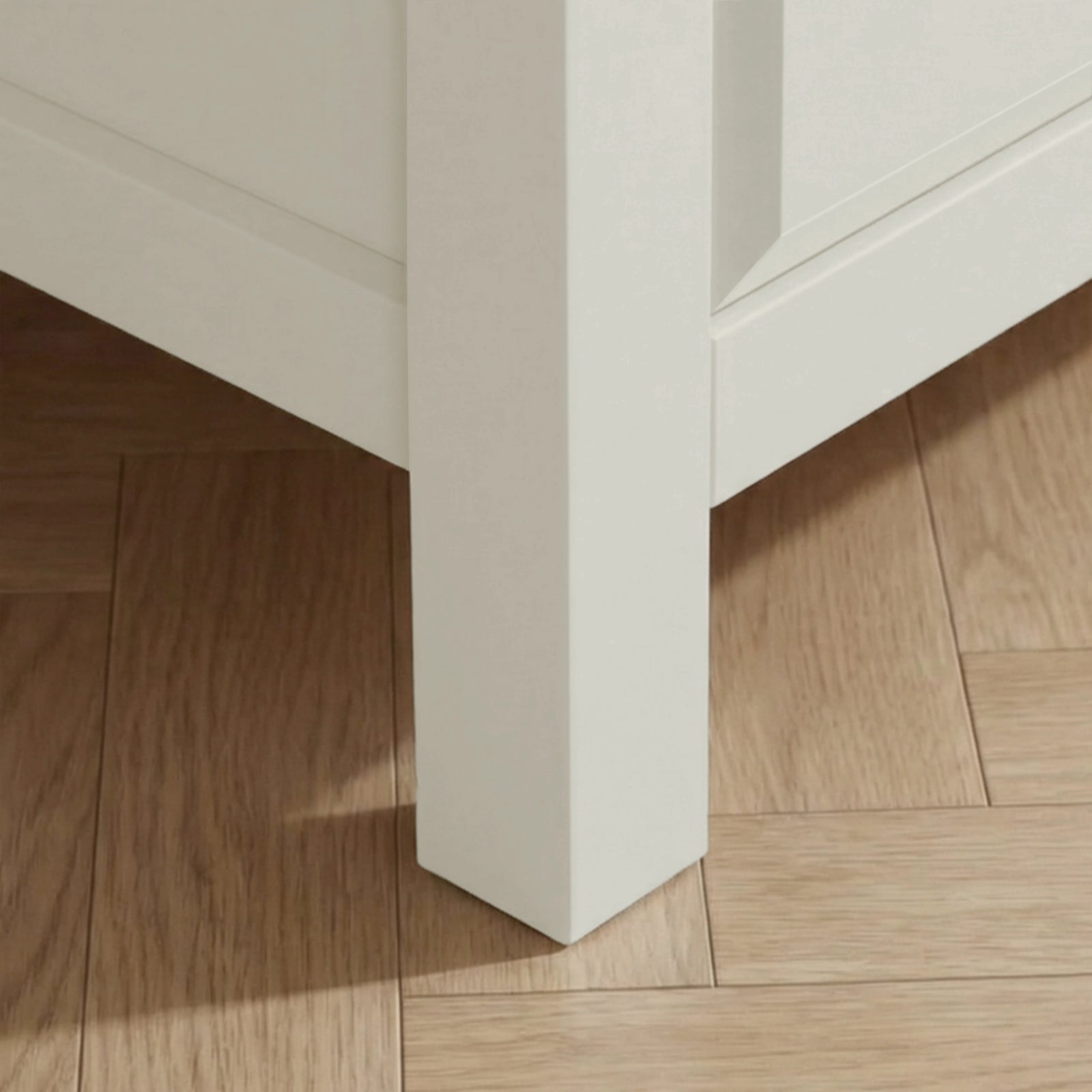[White] Haven chest close-up of the solid square white painted leg resting on warm oak herringbone parquet flooring