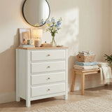 [White] Haven 4 drawer chest in a styled bedroom with a round mirror above, glowing table lamp and blue floral stems