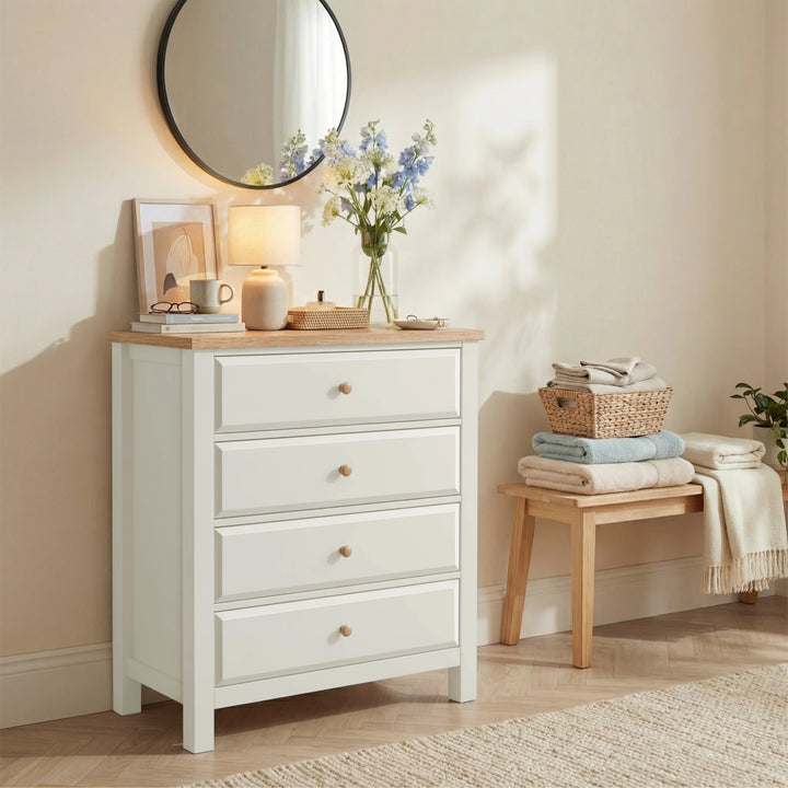 [White] Haven 4 drawer chest in a styled bedroom with a round mirror above, glowing table lamp and blue floral stems