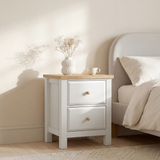 [White] Haven bedside table angled view beside a bed with dried flower vase and cup on the oak top surface