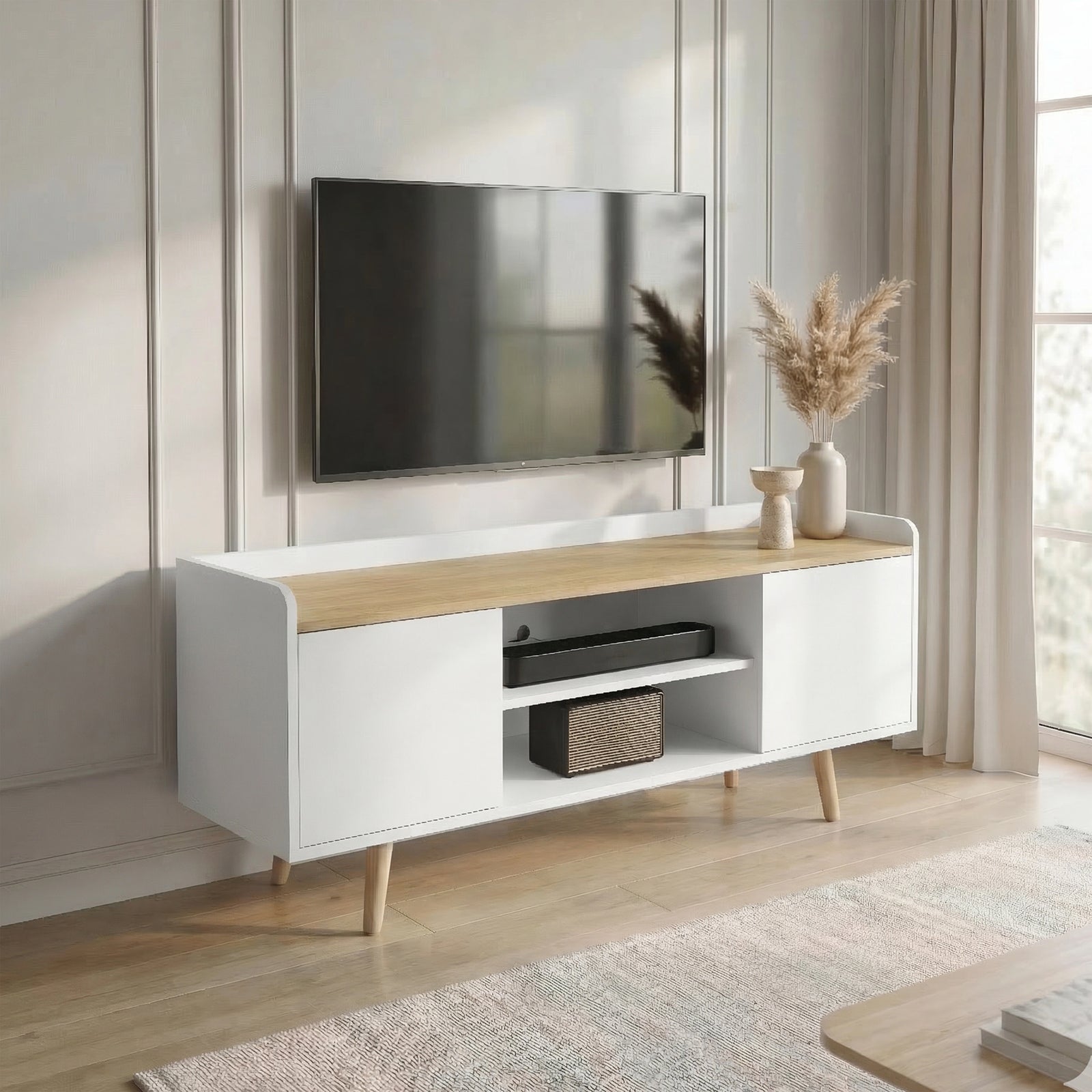 [White | 112 cm] Larvik styled at an angle in a sunlit panelled room with wall-mounted TV, pampas grass, soundbar, and woven speaker