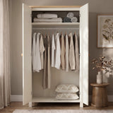 [White] Open wardrobe with clothes and pillows in a room with a wooden stool and plant