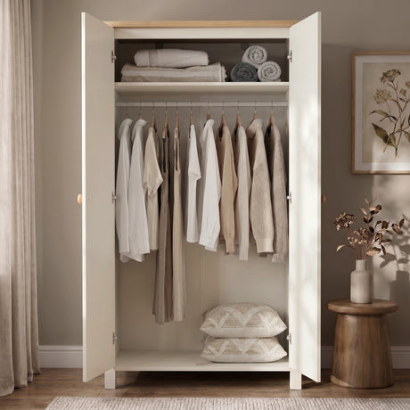 [White] Open wardrobe with clothes and pillows in a room with a wooden stool and plant