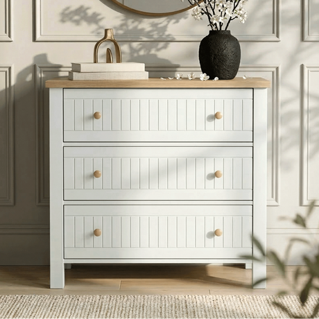 [White] Linra 3-drawer chest of drawers in a lifestyle bedroom setting with mirror and vase on oak top