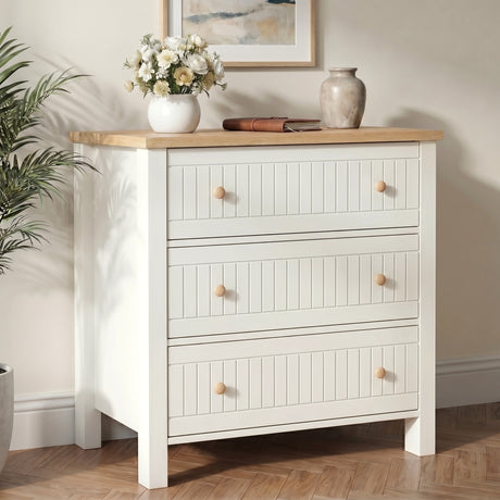 [White] Linra 3 chest of drawers side view with oak top styled with vase, blossom stems, books in sunlight