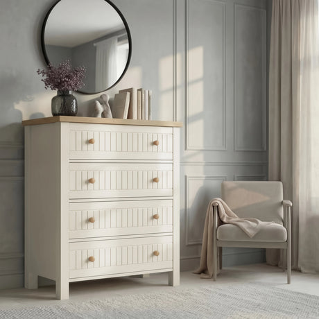 [White] Linra 4 drawer chest in bedroom beside armchair with oak top styled with dried floral vase, ceramic ornament, and stacked books