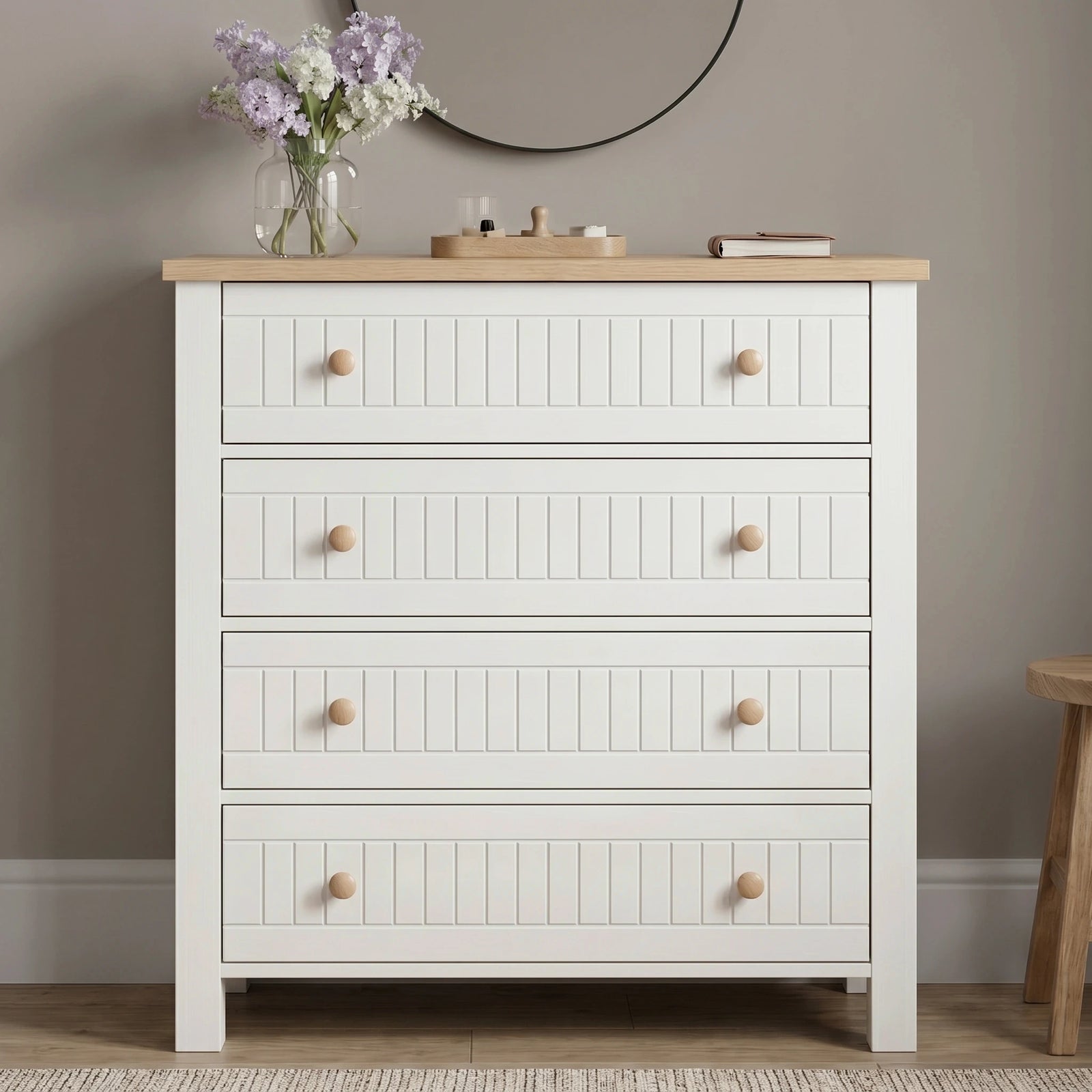 [White] Linra 4 drawer chest front view with oak top styled with dried floral vase, sculptural ornament, and books below a round black mirror