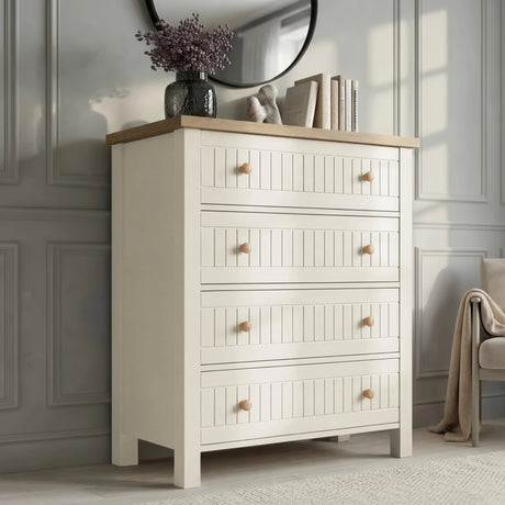 [White] Linra 4 drawer chest angled view with oak top styled with dried floral vase, sculptural ornament, and stacked books below round mirror