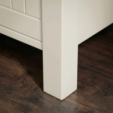 [White] Linra 4 drawer chest close-up of solid square painted leg construction and raised base clearance on dark hardwood flooring