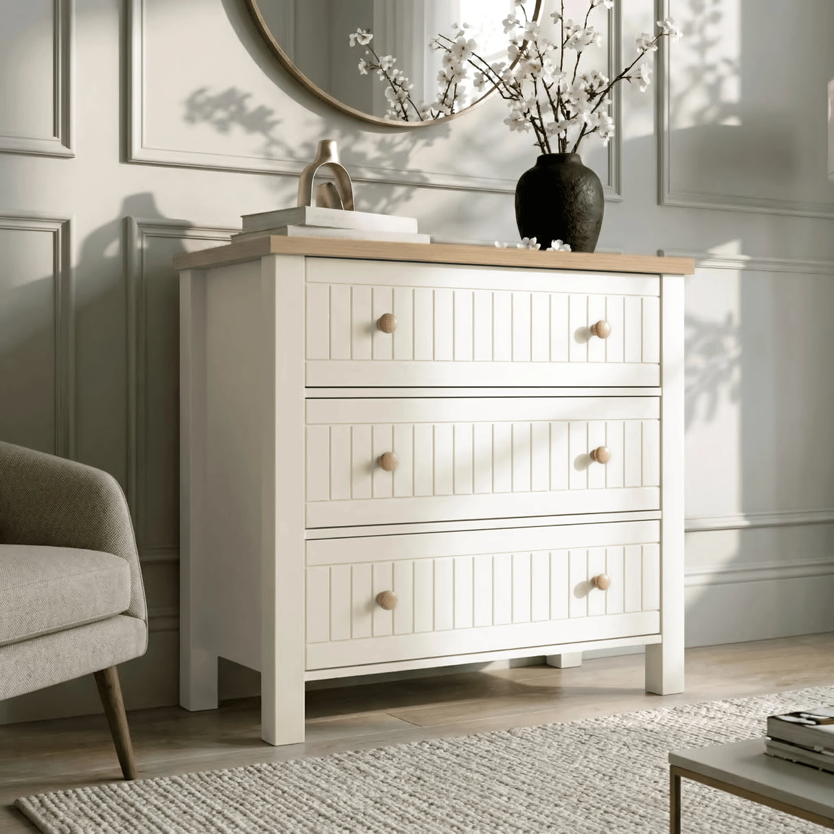 [White] Living space Linra chest of drawers in white beside cream chair with floral vase and gold piece