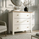 [White] Living space Linra chest of drawers in white beside cream chair with floral vase and gold piece