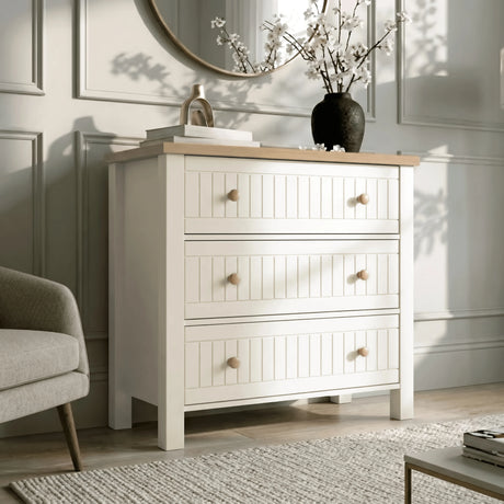 [White] Living space Linra chest of drawers in white beside cream chair with floral vase and gold piece