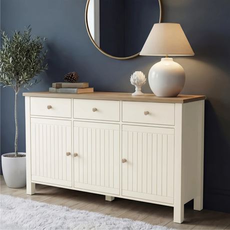 [White] Linra 3 door sideboard front view in dark living space with oak top styled with ceramic lamp, artichoke ornament, and olive tree
