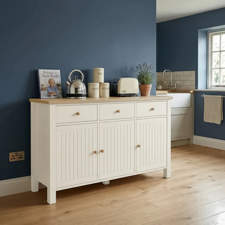 [White] Linra 3 door sideboard used as kitchen storage unit with kettle, toaster, tea and coffee canisters, and cookbook on oak worktop surface