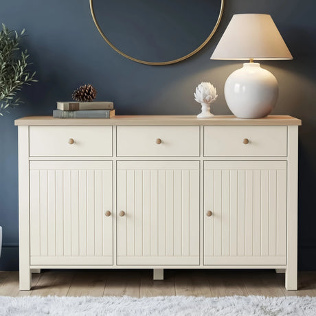 [White] Linra 3 door sideboard front view with oak top styled with ceramic lamp, round mirror, stacked books, and artichoke ornament in living space