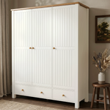 [White] Linra wardrobe angled closed view with beaded doors, lower drawers, oak top, curtain, framed art, vase, and stool.