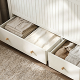 [White] Linra drawer detail showing open lower drawers, folded shirts, knitwear, blanket, wooden knobs, and beaded doors.