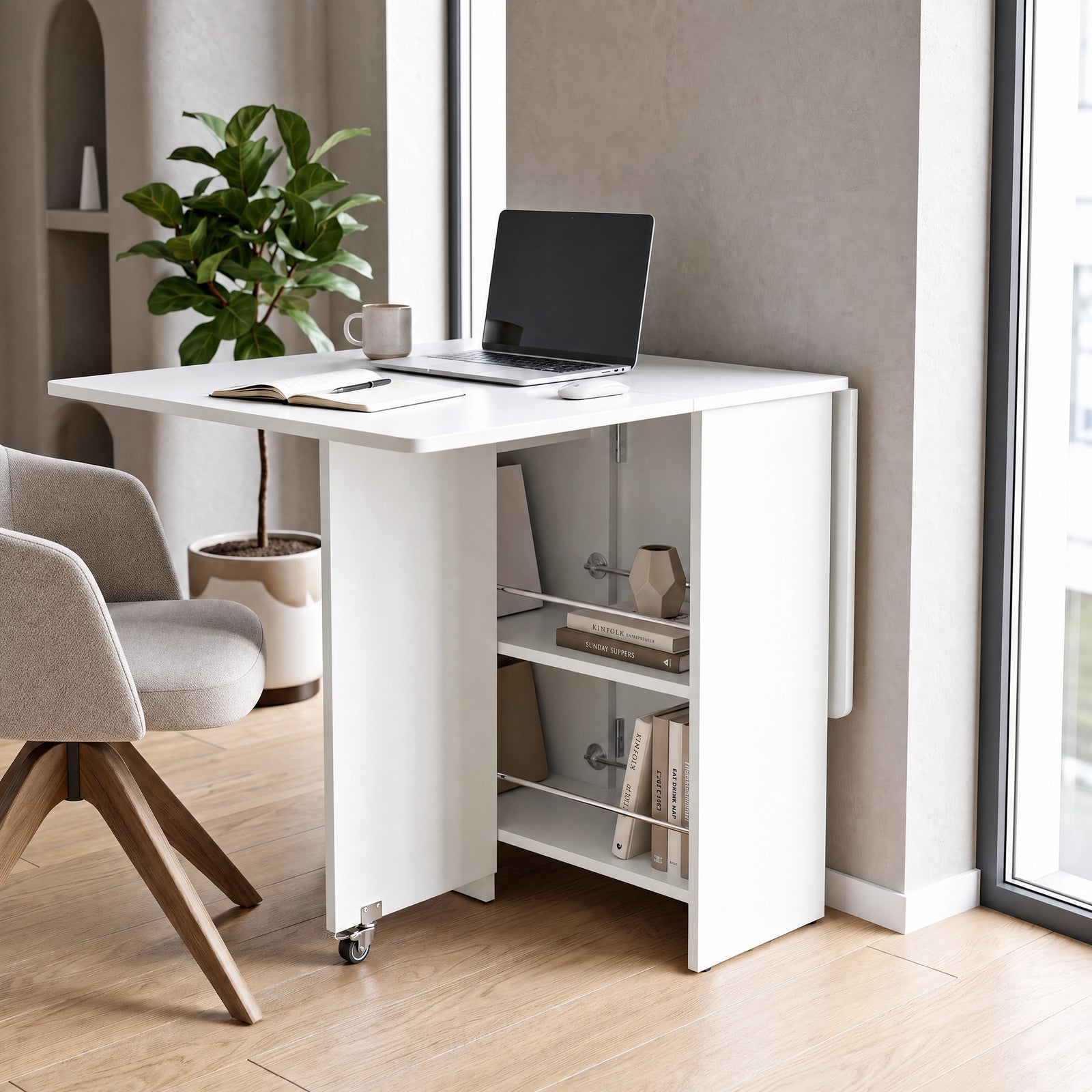 [White] Folding dining table for small space used as a desk with one leaf raised, laptop and rod-fronted shelves on wheels.