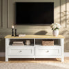 [White] Oskara TV unit front view in living room below wall-mounted TV styled with black candlesticks, hydrangea vase, books, and wicker basket