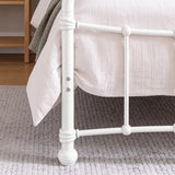 [White | Single] Footboard detail showing two bolts, wrapped rail joints, vertical bar, rounded foot, bedding, and rug.