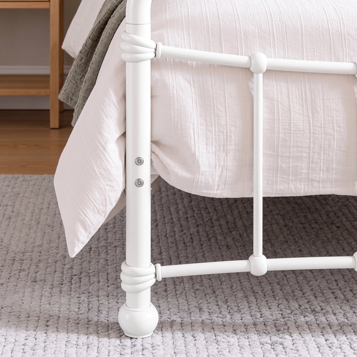 [White | Single] Footboard detail showing two bolts, wrapped rail joints, vertical bar, rounded foot, bedding, and rug.