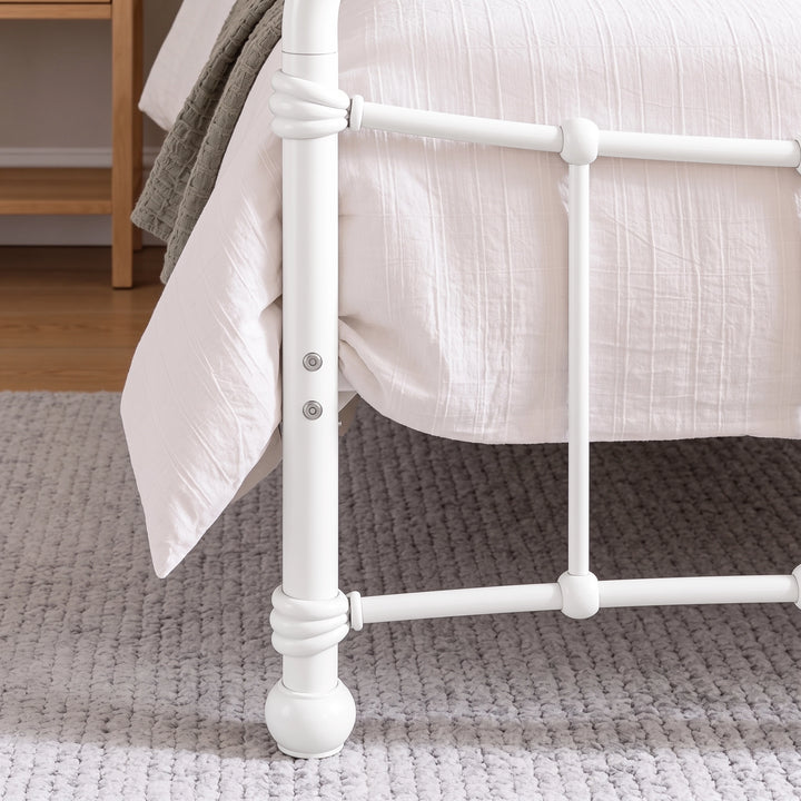 [White | Single] Footboard detail showing two bolts, wrapped rail joints, vertical bar, rounded foot, bedding, and rug.