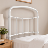[White | Single] Headboard close-up showing curved rail, vertical bars, rounded joints, bedding, bedside plant, and lamp.