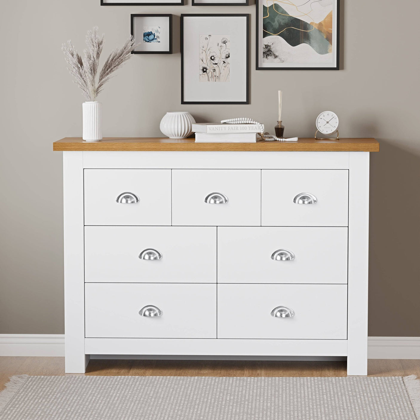 White tall chest of drawers with sleek top, displaying a watch, books, and flower pots.
