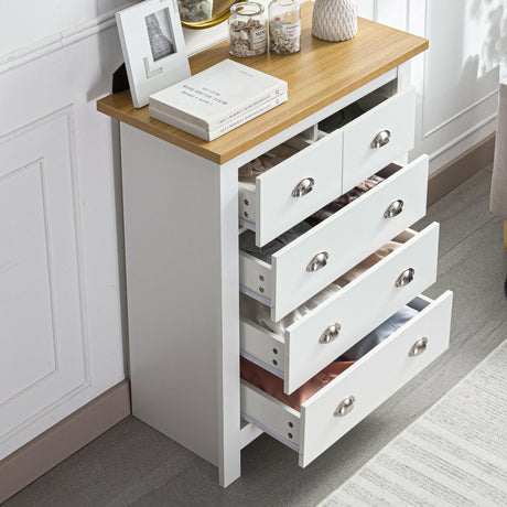 White tall chest of drawers with sleek top, displaying a watch, books, and flower pots.
