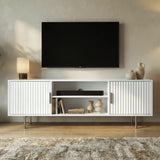 Modern white TV entertainment unit featuring fluted cabinet doors, open shelving, and sleek silver metal legs.