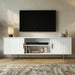 Modern white TV entertainment unit featuring fluted cabinet doors, open shelving, and sleek silver metal legs.
