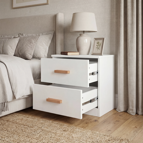 White two drawer bedside table positioned in bedroom corner with lamp and framed wall art on a wooden flooring