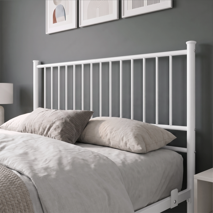 [White | Double] Metal bed close-up view of tall white bar headboard, layered neutral pillows, side rail and mattress stop.