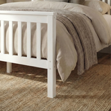 Close up view of white wooden double bed frame slatted footboard with beige bedding on a wooden floor