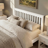 [White | Double] wooden double bed frame slatted headboard view, cream lamps flanking stacked beige pillows