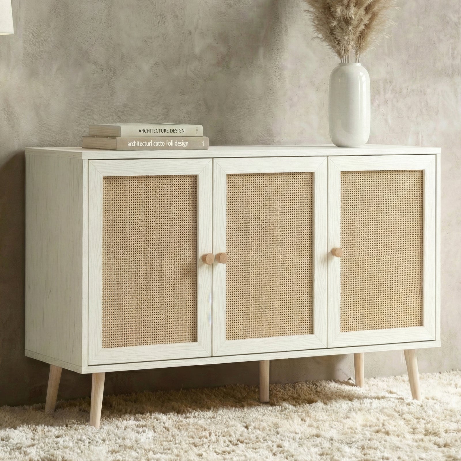 [White] Wovena rattan 3 door sideboard front lifestyle, pampas vase and books on top, on cream rug by grey wall