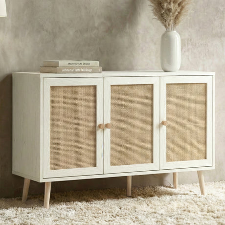 [White] Wovena 3-door sideboard in a closer front lifestyle view against a grey wall, topped with stacked books and a white vase of pampas grass on a fluffy rug