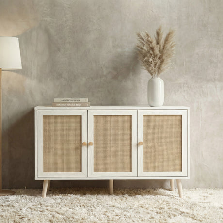 [White] Wovena 3-door sideboard seen from above in a textured grey room with stacked books, a white vase of pampas grass, and a floor lamp to the left